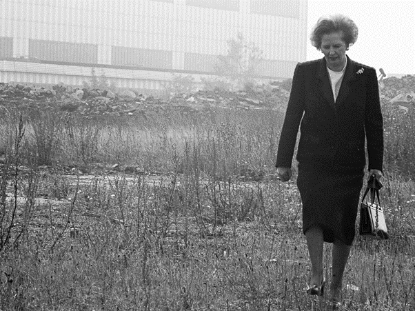 Ikonická fotografia britskej premiérky Margater Thatcher, prechádzajúcej sa pláňami skrachovaných fabrík. 