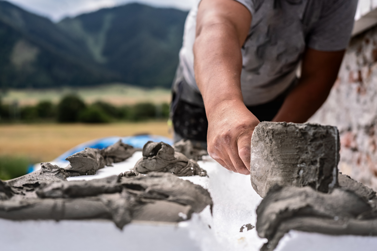 Installing white polystyrene heat insulation, detail on worker hand putting gray bonding cement glue on white boards