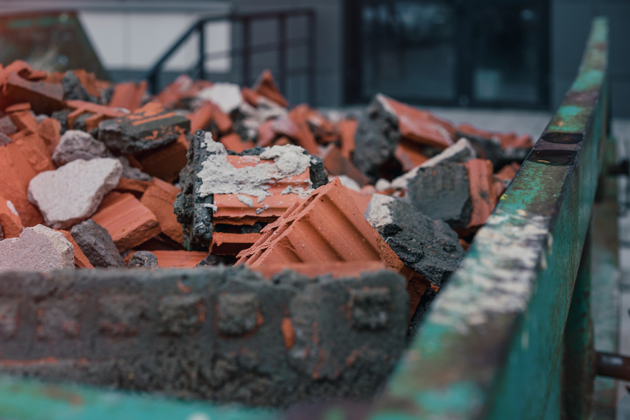 Green metal skip full of broken brick and stone material on construction site