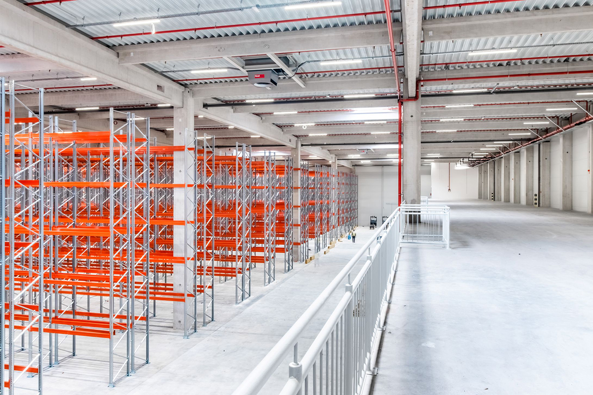 Montáž skladovacích regálov v logistickej hale s vysokou svetlou výškou a technickou infraštruktúrou