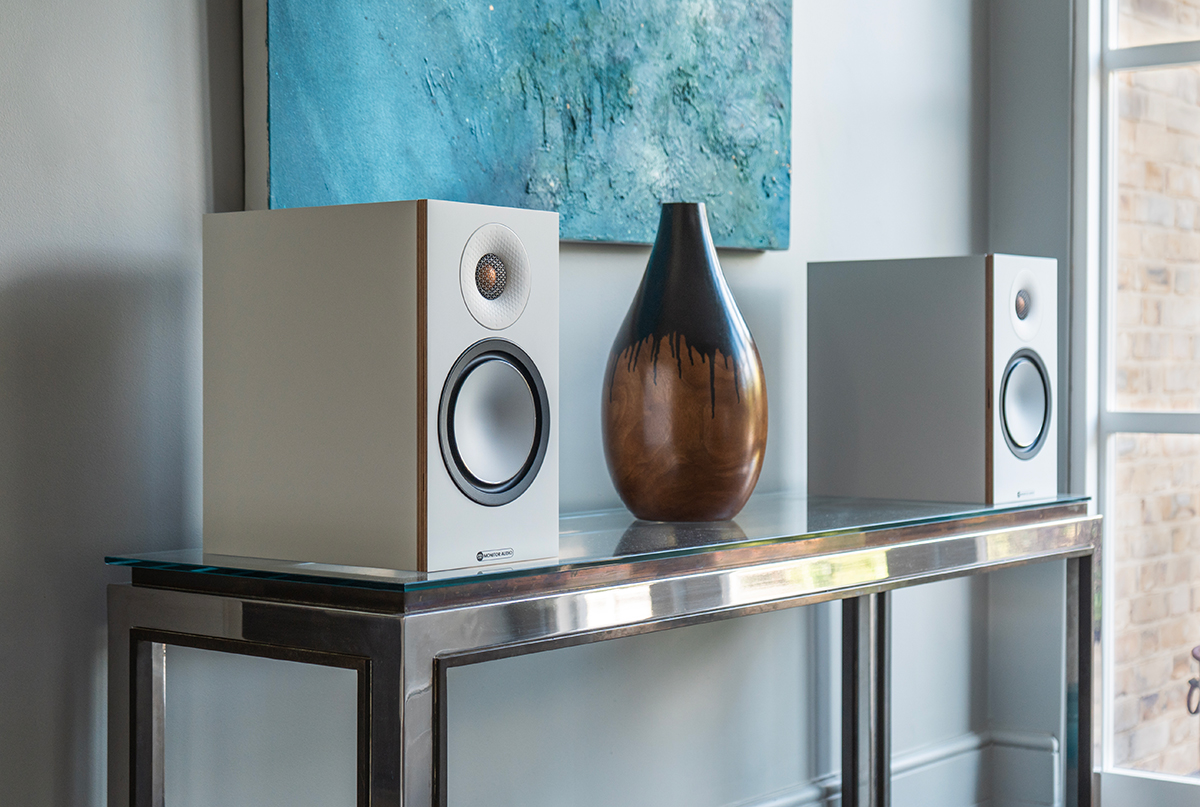Regálové reproduktory Monitor Audio Bronze 50 7G v bielej farbe na sklenenom stole s dekoráciou