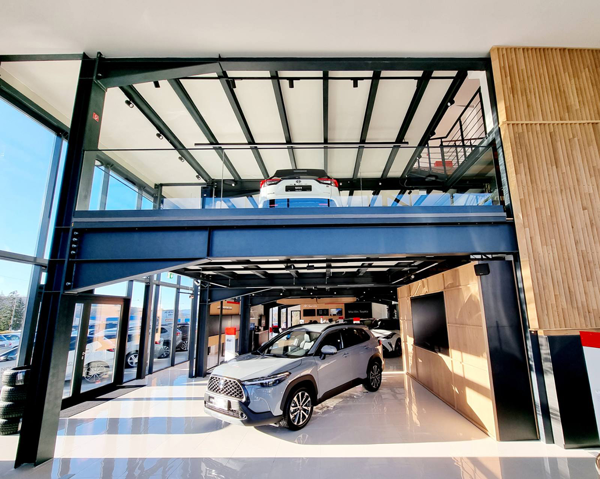 Interiér autosalonu s ocelovou konstrukcí a vystavenými vozy – dvoupatrový showroom s moderním designem.