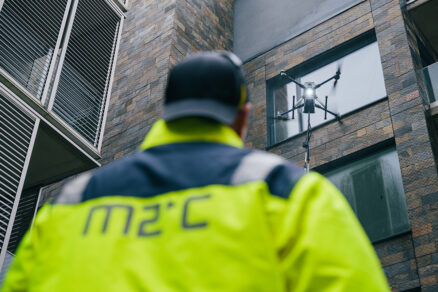 Operátor riadi dron počas čistenia sklenenej fasády moderného objektu