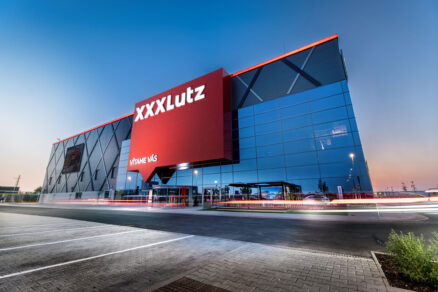 Sklenená fasáda nového obchodného domu s logom XXXLutz v Nitre počas večera