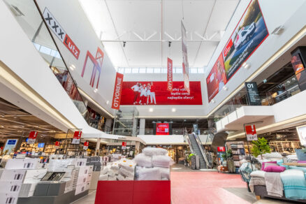 Spodný pohľad na svetlé dvojpodlažné átrium s červenými vizuálmi a eskalátormi