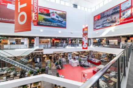 Spodný pohľad na svetlé dvojpodlažné átrium s červenými vizuálmi a eskalátormi