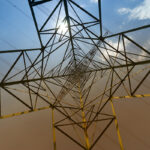 Pohľad zdola na oceľový stožiar elektrického vedenia pri modrej oblohe – symbol modernej energetickej infraštruktúry.