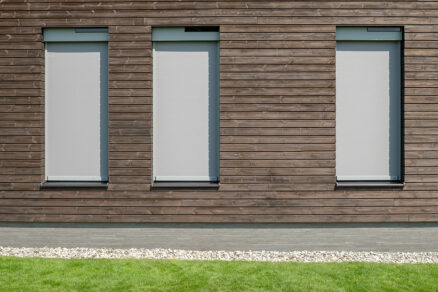 Tri rovnaké screenové rolety na modernom dome s dreveným obkladom