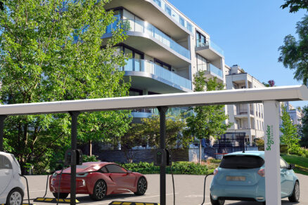 Vonkajšie nabíjacie stanice pre elektromobily v obytnom komplexe so strieškou a označením Schneider Electric