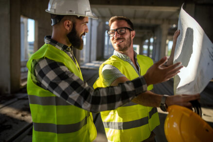 Dvaja stavební inžinieri na stavbe konzultujú výkresy počas technického dozoru