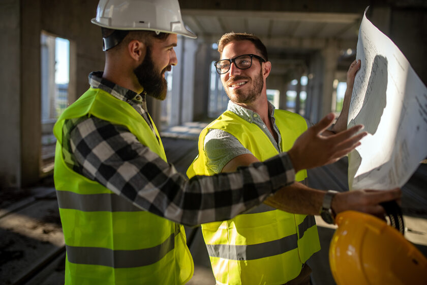 Dvaja stavební inžinieri na stavbe konzultujú výkresy počas technického dozoru