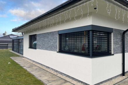 Rohový pohľad na rodinný dom s čiernymi vonkajšími žalúziami a sivým obkladom