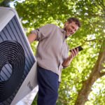 muž ovláda tepelné čerpadlo cez smartfón pri vonkajšej jednotke