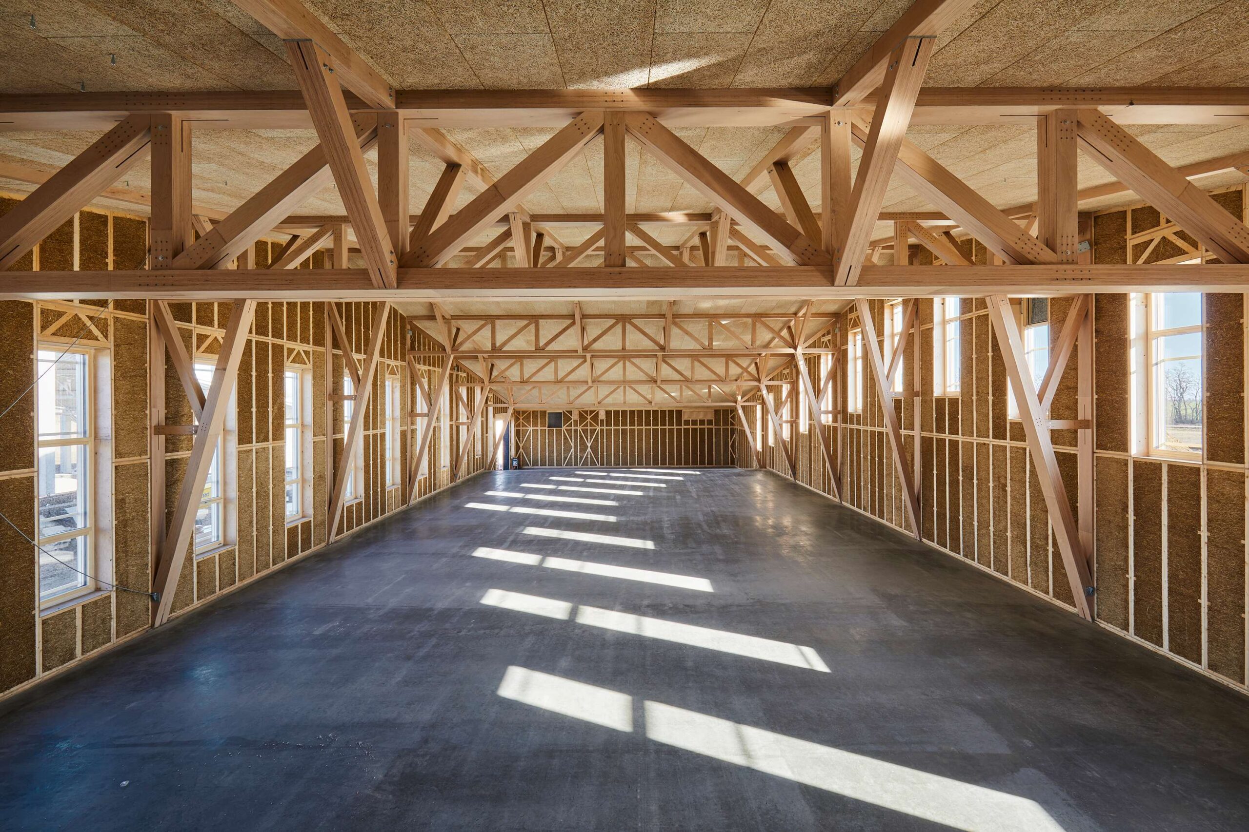 Odhalené drevené konštrukcie a slamené panely tu netvoria len stavebnú obálku, ale stávajú sa samotným vizuálnym a estetickým zážitkom z architektúry. vyrobna-hala-voderady