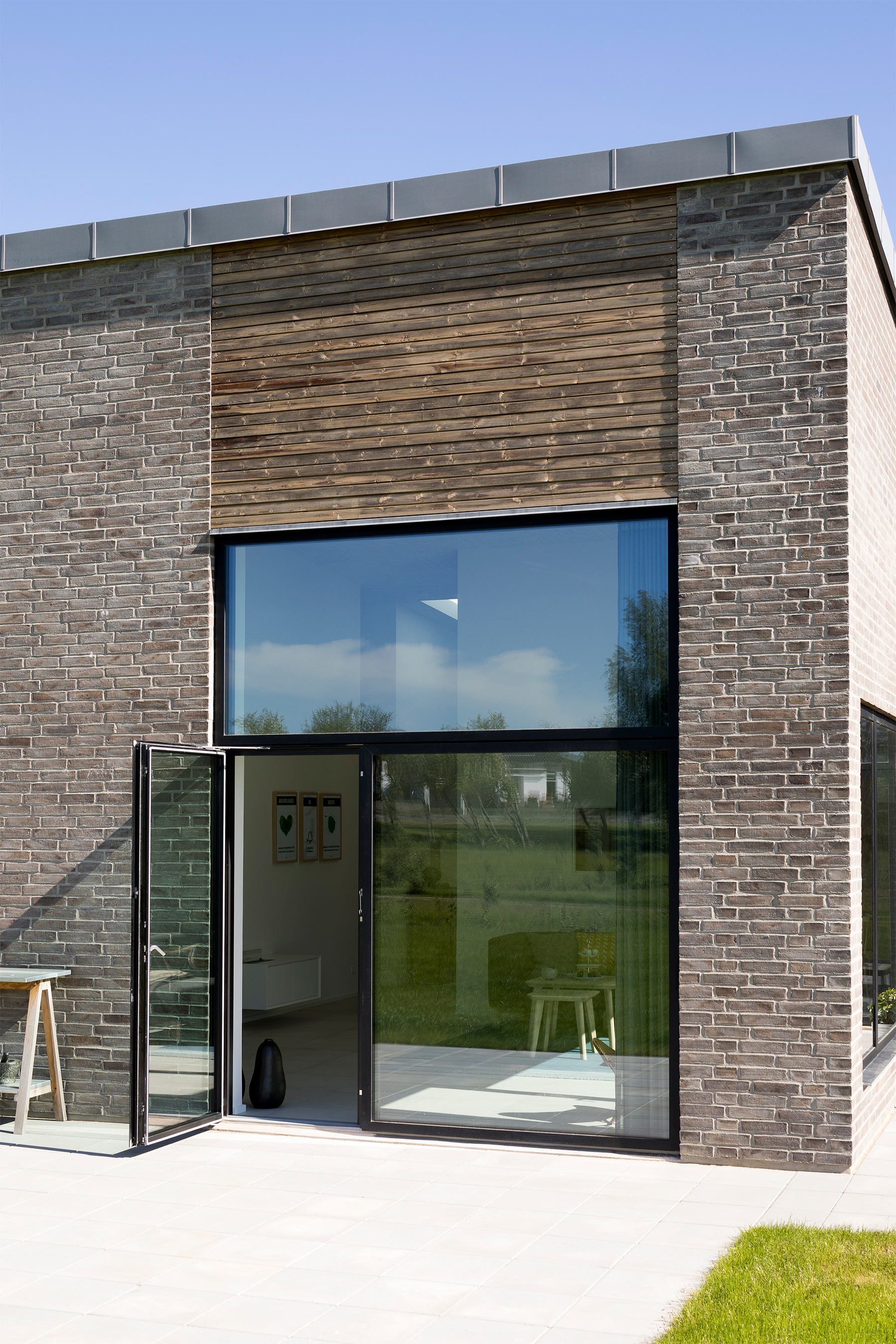 Textúra tehlovej fasády je v kontraste s drevenými profilmi a čiernymi rámami okien a dverí.